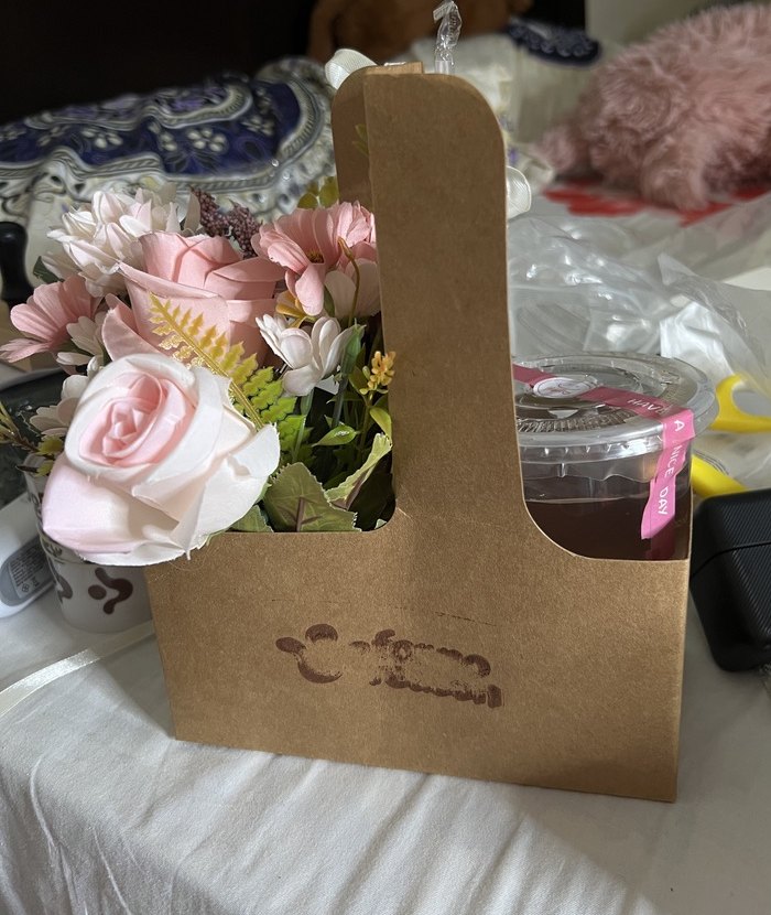 A kraft carrier holding a bouquet on one side and a sealed drink on the other
